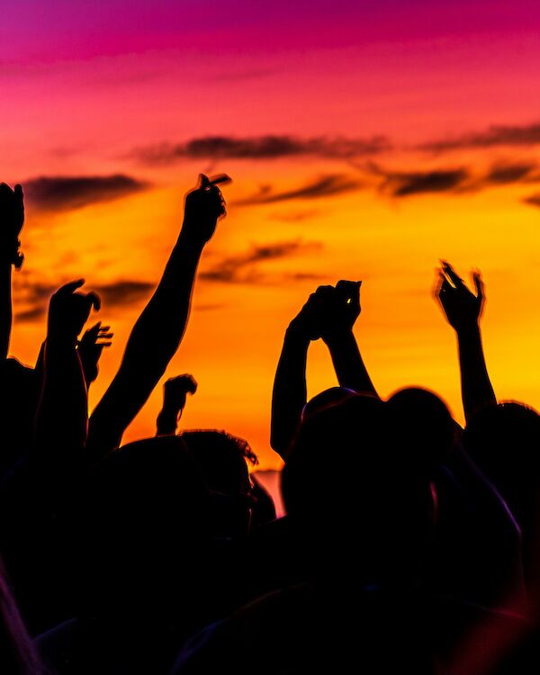 Silhouetted crowd with raised hands against a vibrant sunset sky, creating an energetic atmosphere.