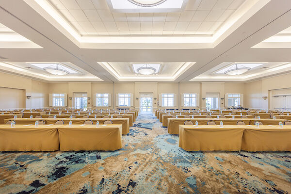 A conference room with arranged tables, chairs, and water bottles on a patterned carpet under a well-lit ceiling.