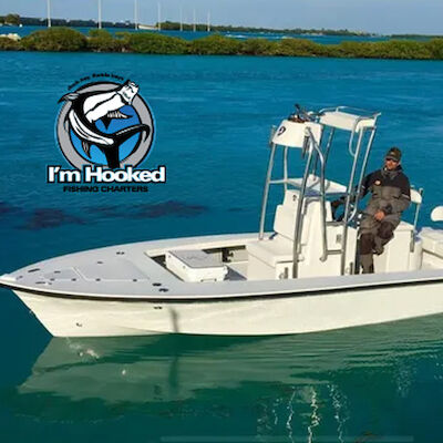 A person is sitting on a white boat in turquoise water with "I'm Hooked Fishing Charters" logo visible in the image.