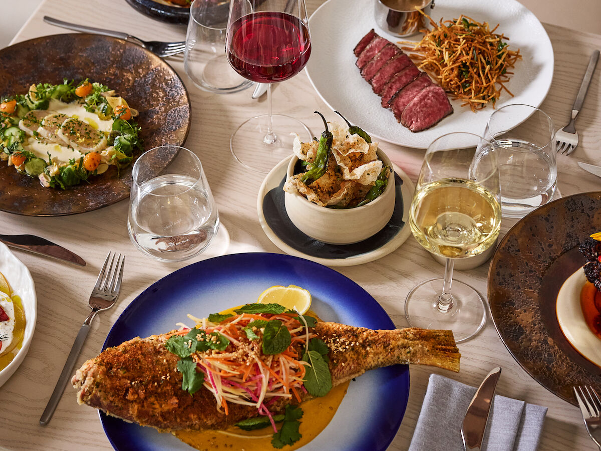A table set with gourmet dishes including fish, steak, pasta, vegetables, and wine glasses, creating an elegant dining experience.