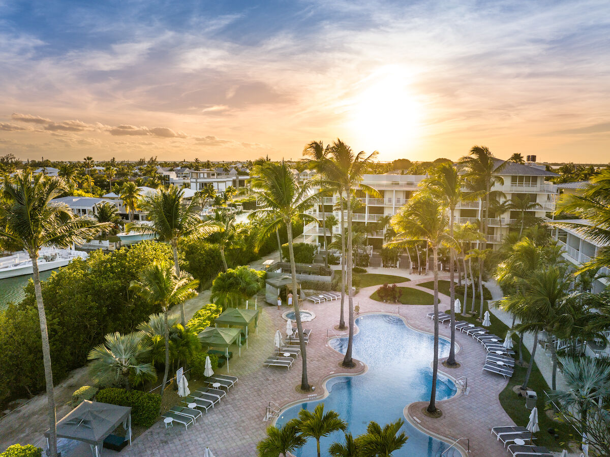 A serene aerial view of a tropical resort with a pool, palm trees, and sunset, offering a relaxing vacation atmosphere.