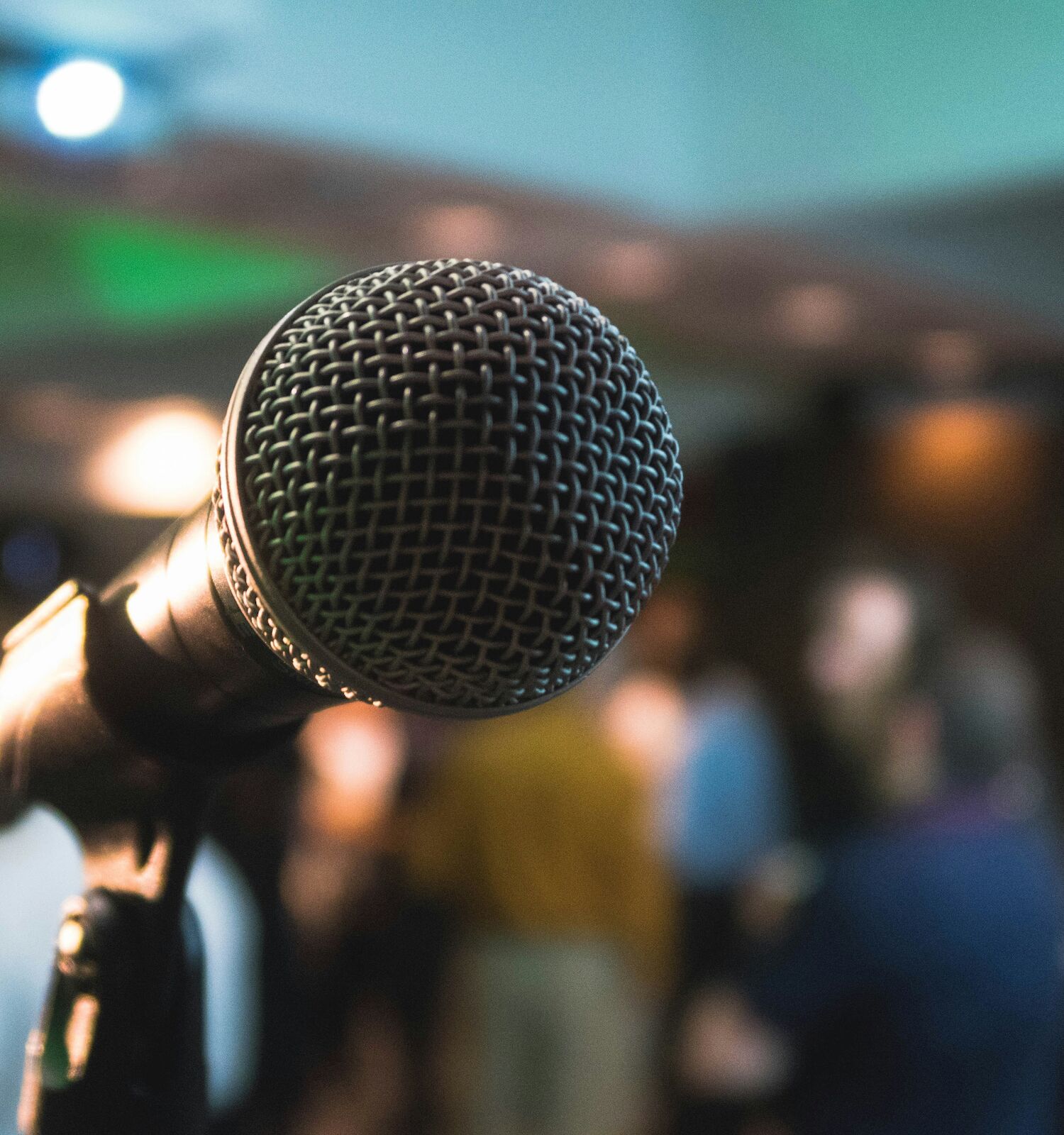 A close-up of a microphone with a blurred background of people gathered in a room, likely an event or performance setting.