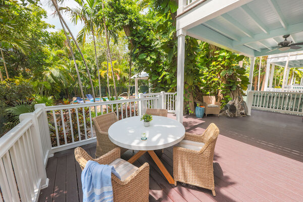 A lush patio with a round table, wicker chairs, and tropical plants, offering a serene outdoor space for relaxation.